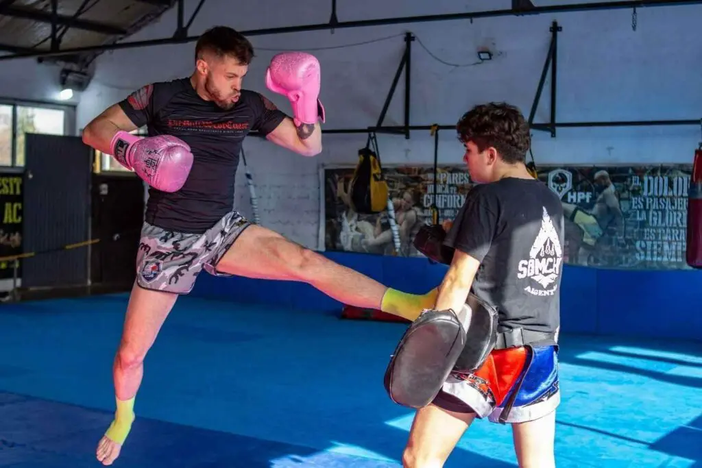 Muay Thai student throwing a front kick into focus pads during partner drills while building Muay Thai fundamentals for beginners.