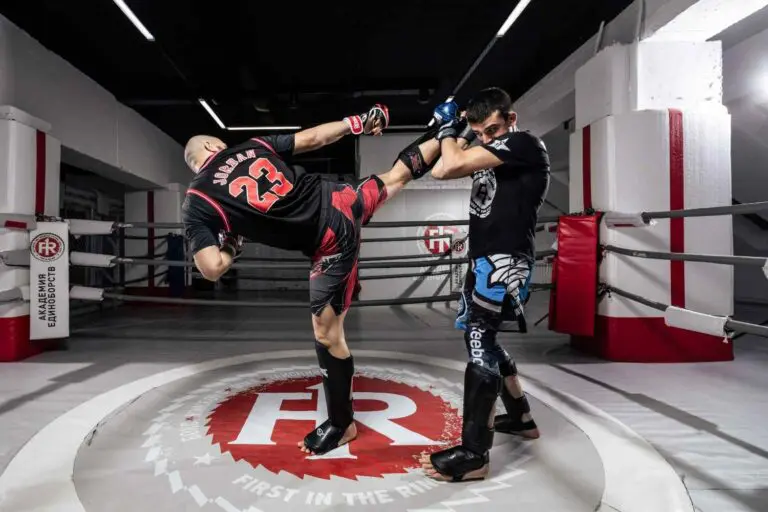 Muay Thai fighter throwing a high roundhouse kick while an opponent blocks in the ring during sparring, Muay Thai clinch for beginners