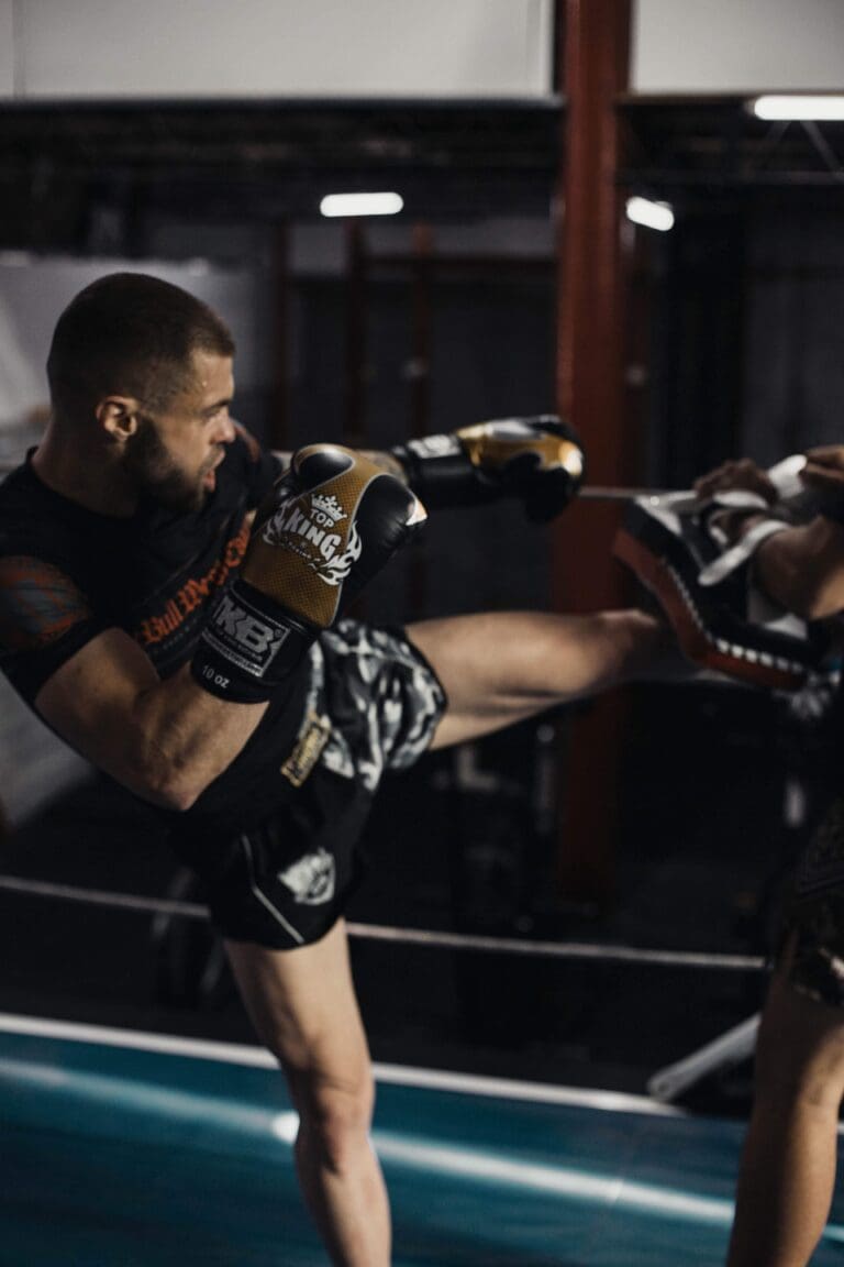 Male kickboxing student practicing a powerful roundhouse kick on a trainer&rsquo;s pad during striking drills, kickboxing vs other martial arts.